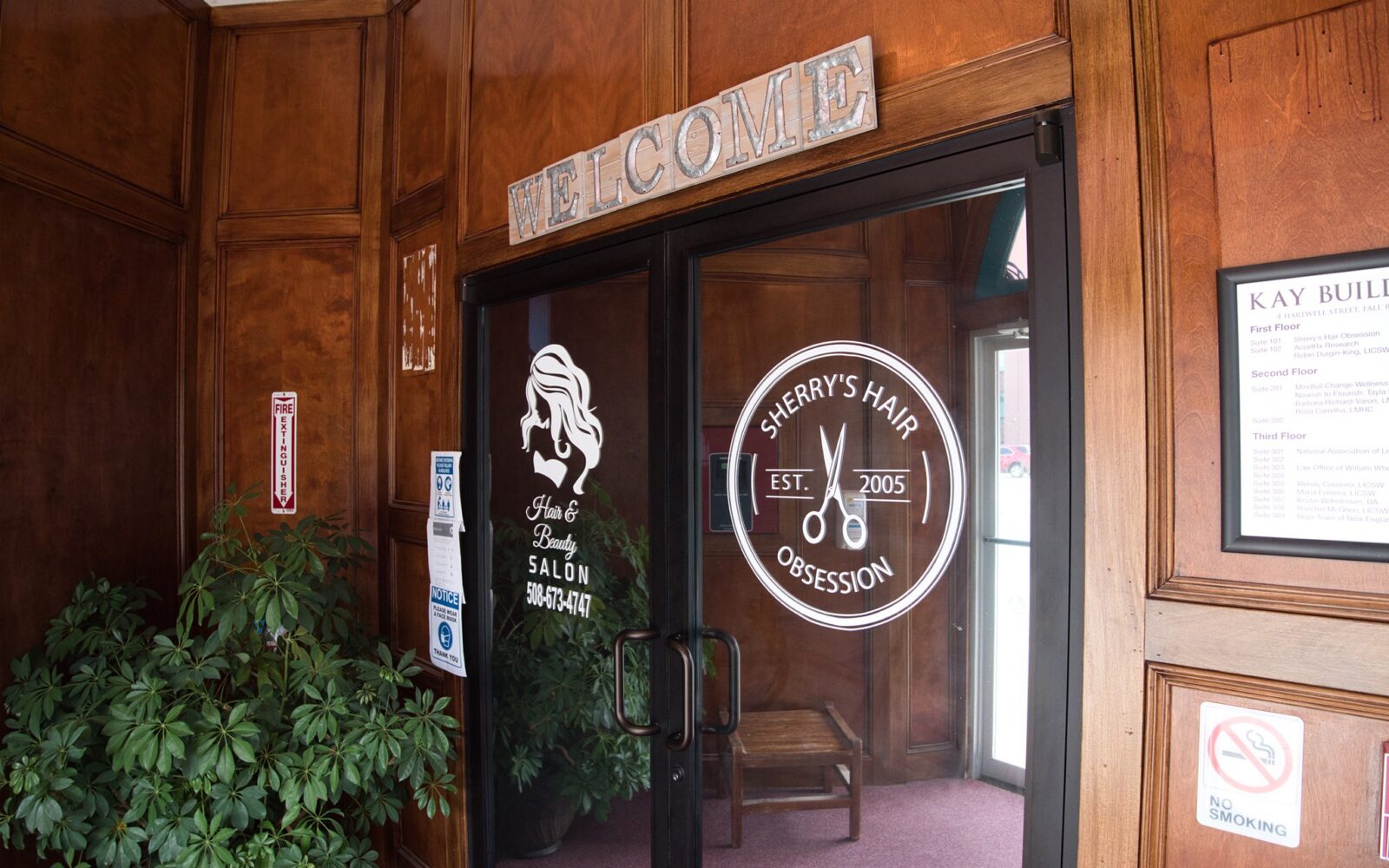 Entrance to Sherry's Hair Obsession salon with wooden walls and plants. Welcome sign above the door.