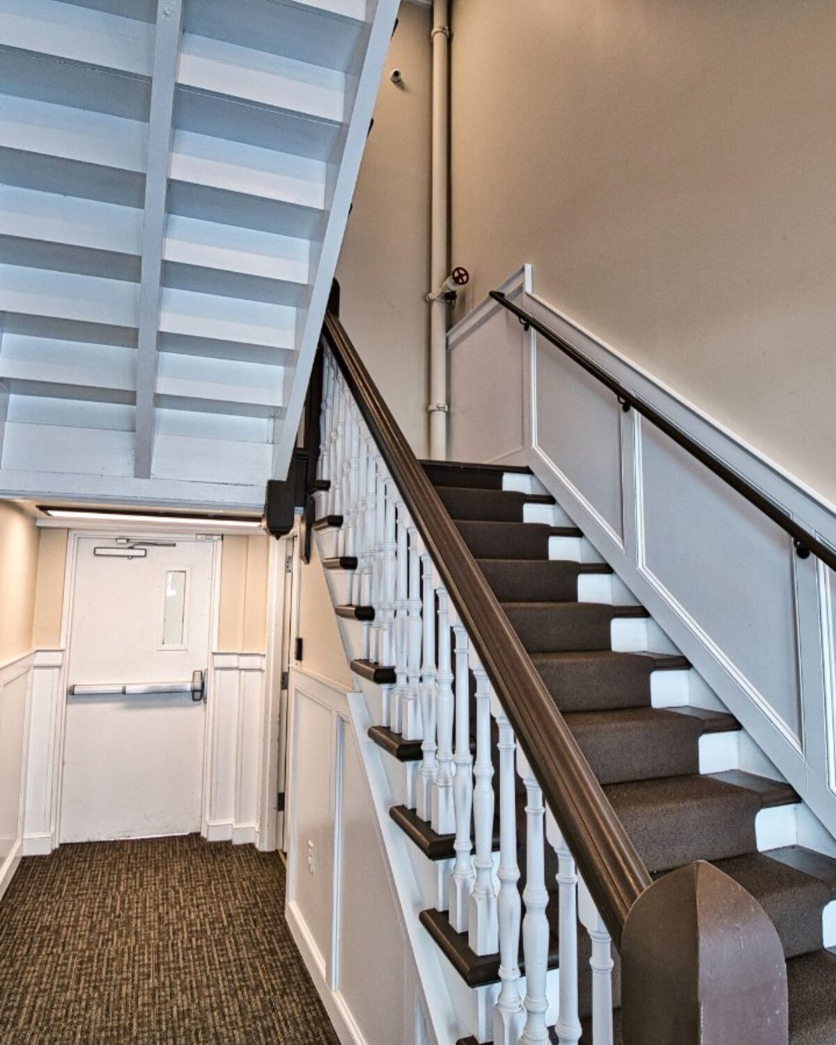 Staircase with white railings and a door at the end of a hallway.
