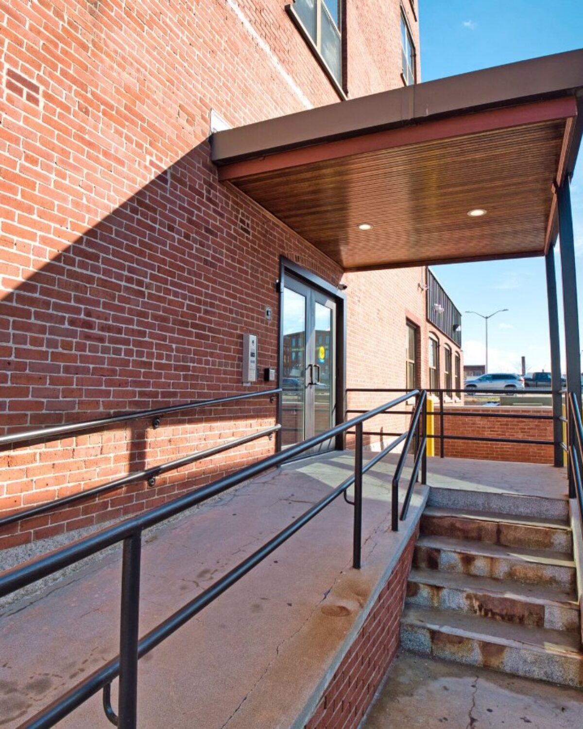 Entrance with a ramp and stairs, featuring a door and a handicap parking sign nearby.