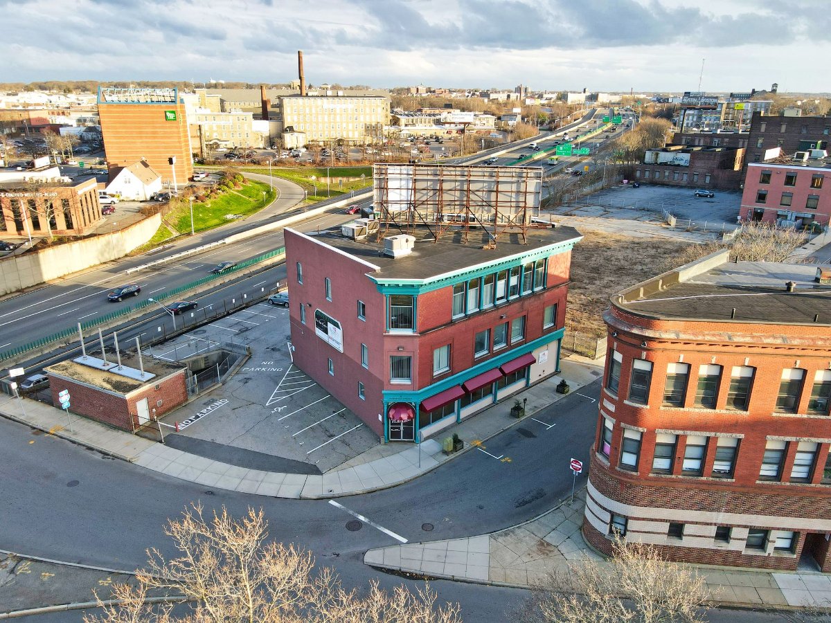 Aerial view of a red brick building with a sign, surrounded by roads and vacant lots.