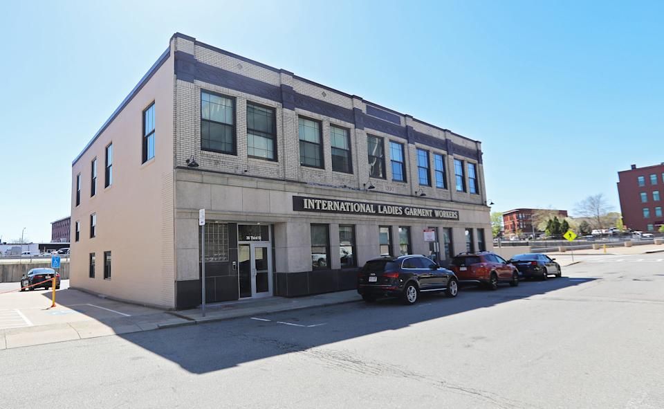 Historic building labeled "International Ladies Garment Workers" with parked cars nearby. Clear blue sky above.