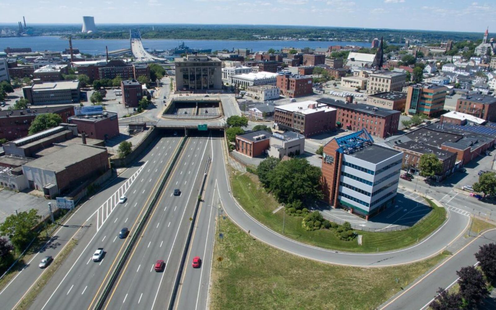 Aerial view of a city with a highway, buildings, and a river in the background.